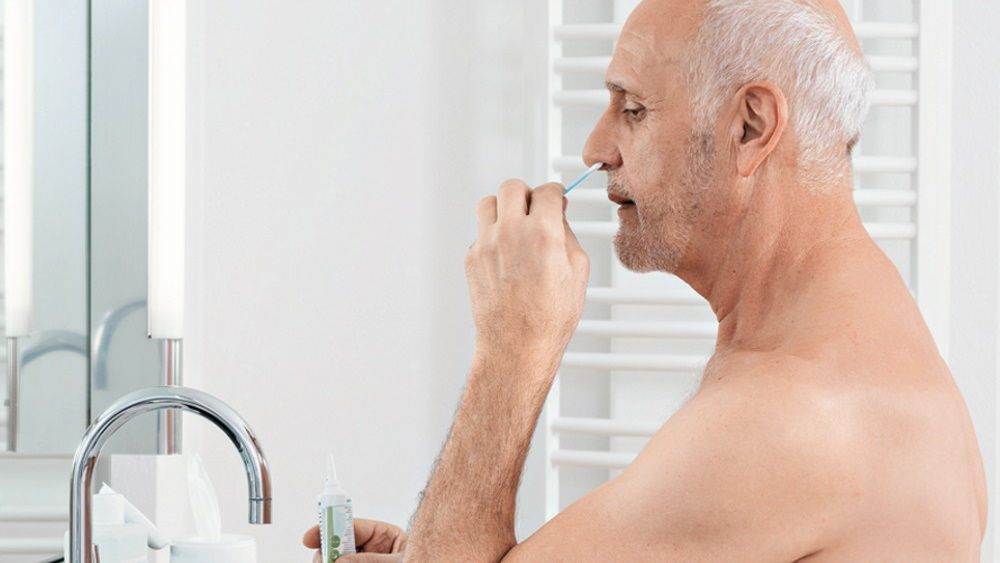 oudere man die thuis voor de badspiegel een antimicrobiële neusspoeling uitvoert 