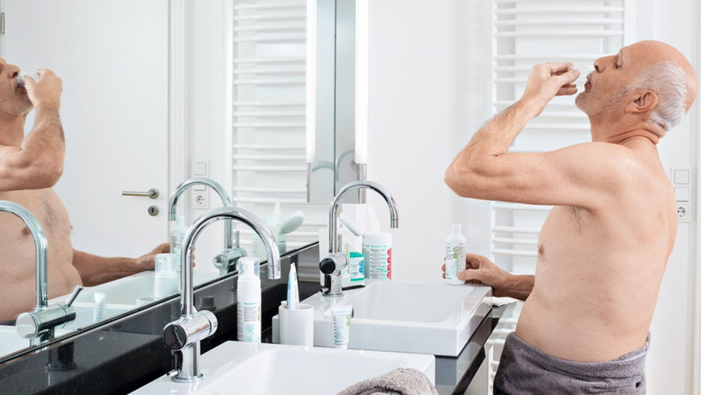 oudere man die thuis voor de badspiegel een antimicrobiële mondspoeling uitvoert 