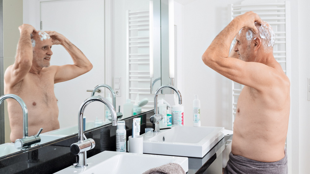 oudere man doet thuis een antimicrobiële haarwas voor de badspiegel 